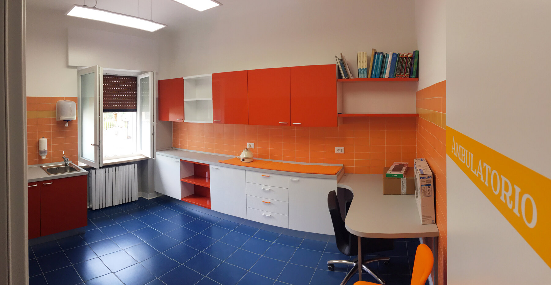 Vista d’insieme dell’ambulatorio arancio, con il piano visita e la postazione di refertazione