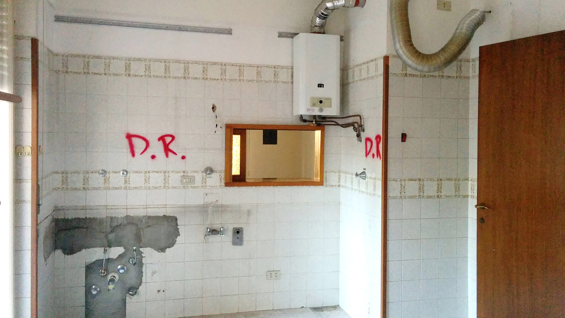 La cucina svuotata, con i tracciamenti a parete che segnano le demolizioni